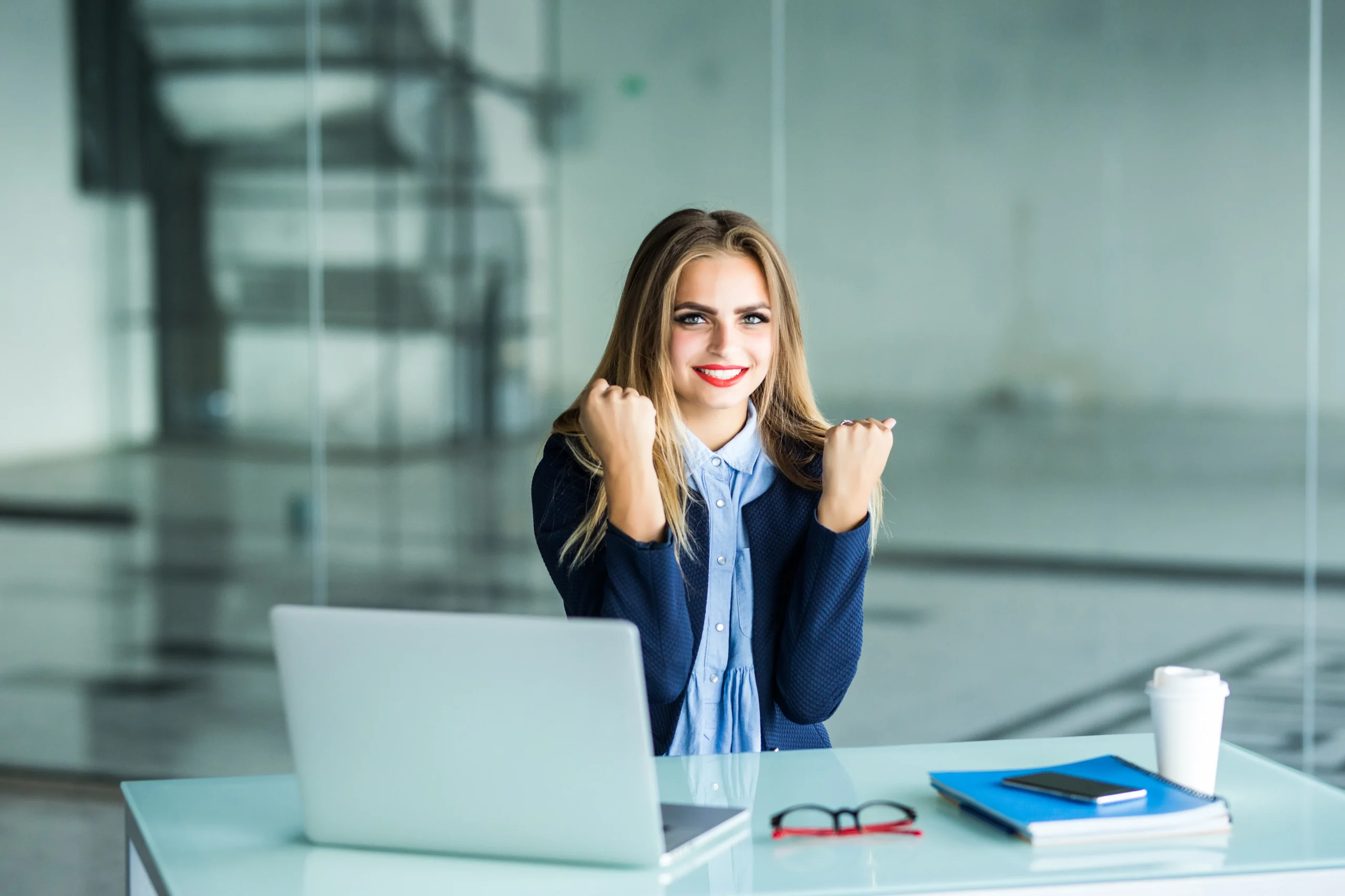 excited businesswoman winning after achievement reading smart phone sitting desktop office
